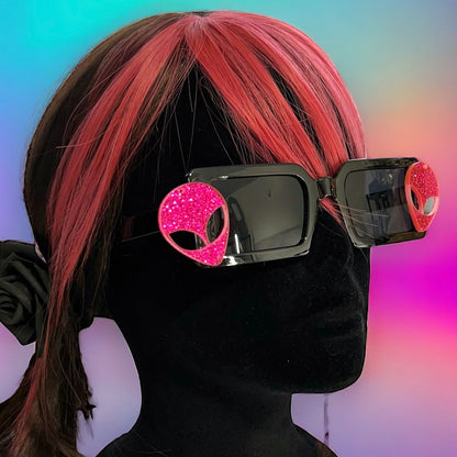 Hot Pink Alien Sunglasses with black frames and glittery pink aliens on sides – a bold and cosmic accessory for festivals and raves. Square/rectangle shape. Displayed on a mannequin.