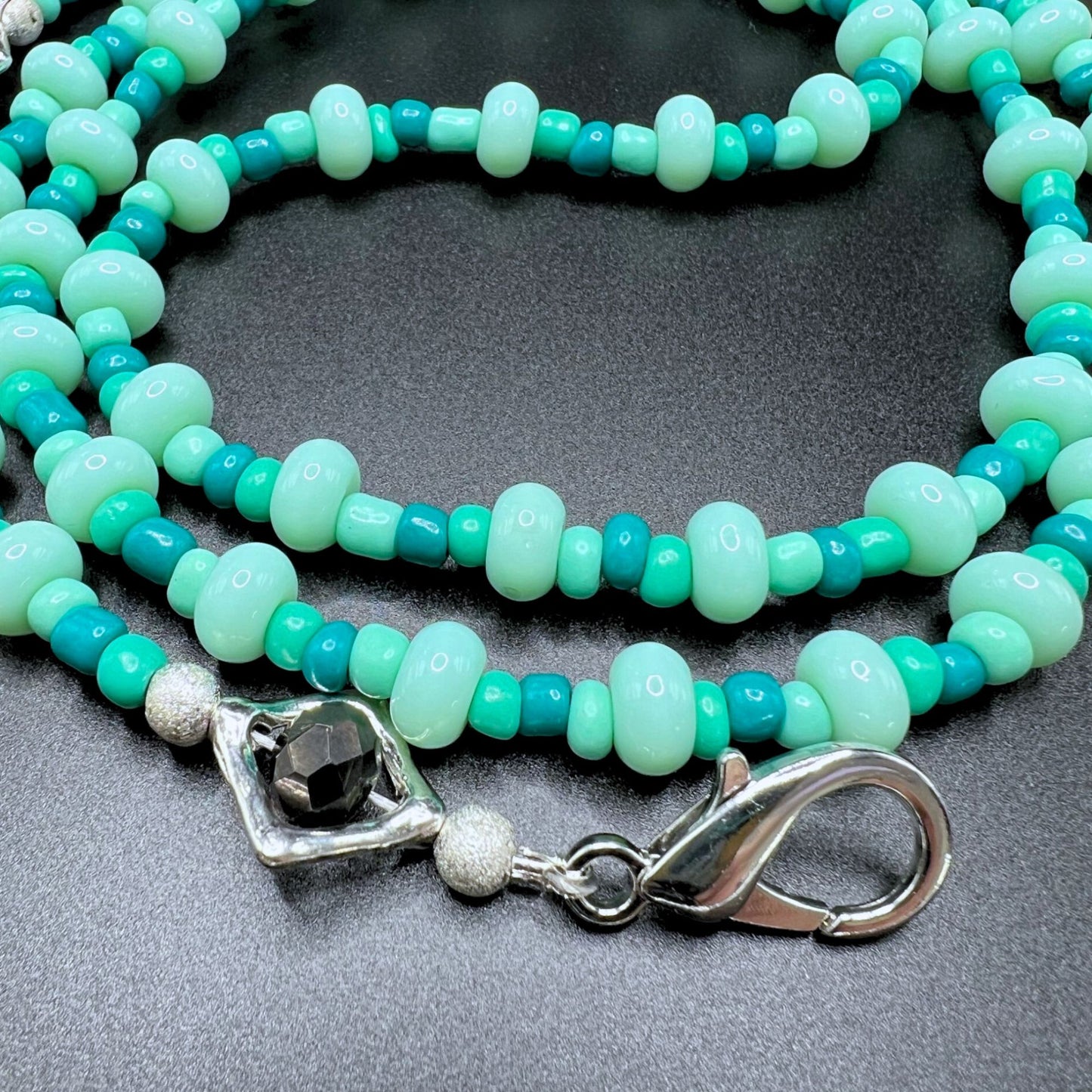 Mint blue and green beaded glasses chain with silver-tone clasps. Displayed on a table.