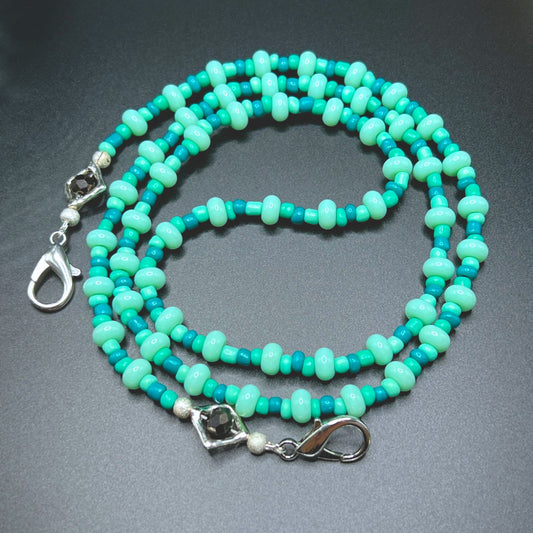 Mint blue and green beaded glasses chain with silver-tone clasps. Displayed on a table.