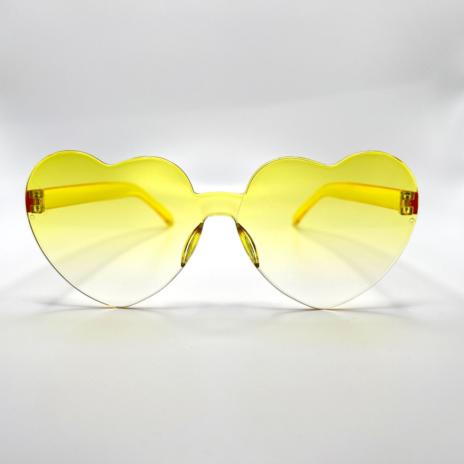 Colorful oversized heart-shaped sunglasses, perfect for festivals and dancing. Lightweight and trendy eyewear for a vibrant and stylish look. Displayed on a table. Front view. Yellow Ombre Heart.