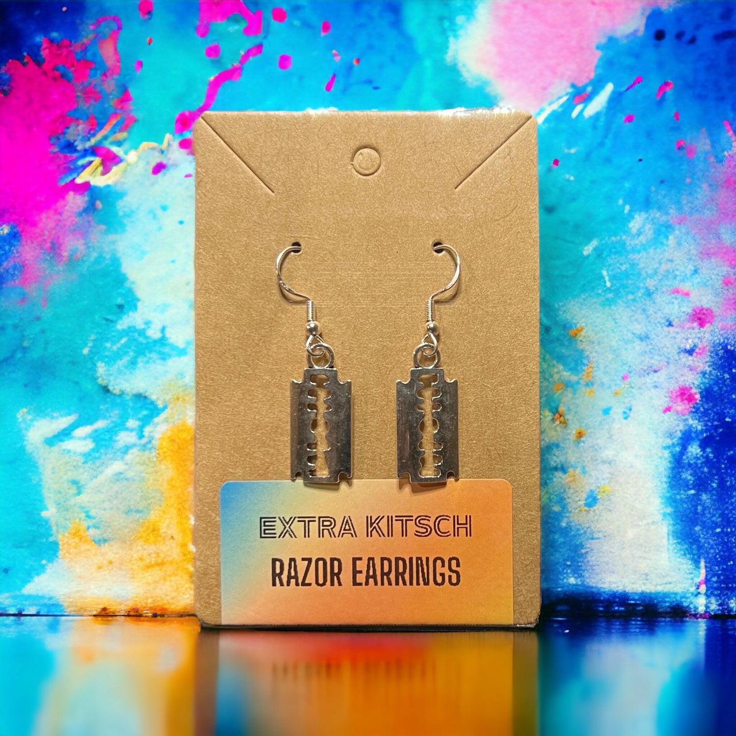 Silver tone razor blade charm earrings, inspired by punk and goth fashion. Displayed on the Extra Kitsch branded merchandise card. Makes it perfect for gift giving.