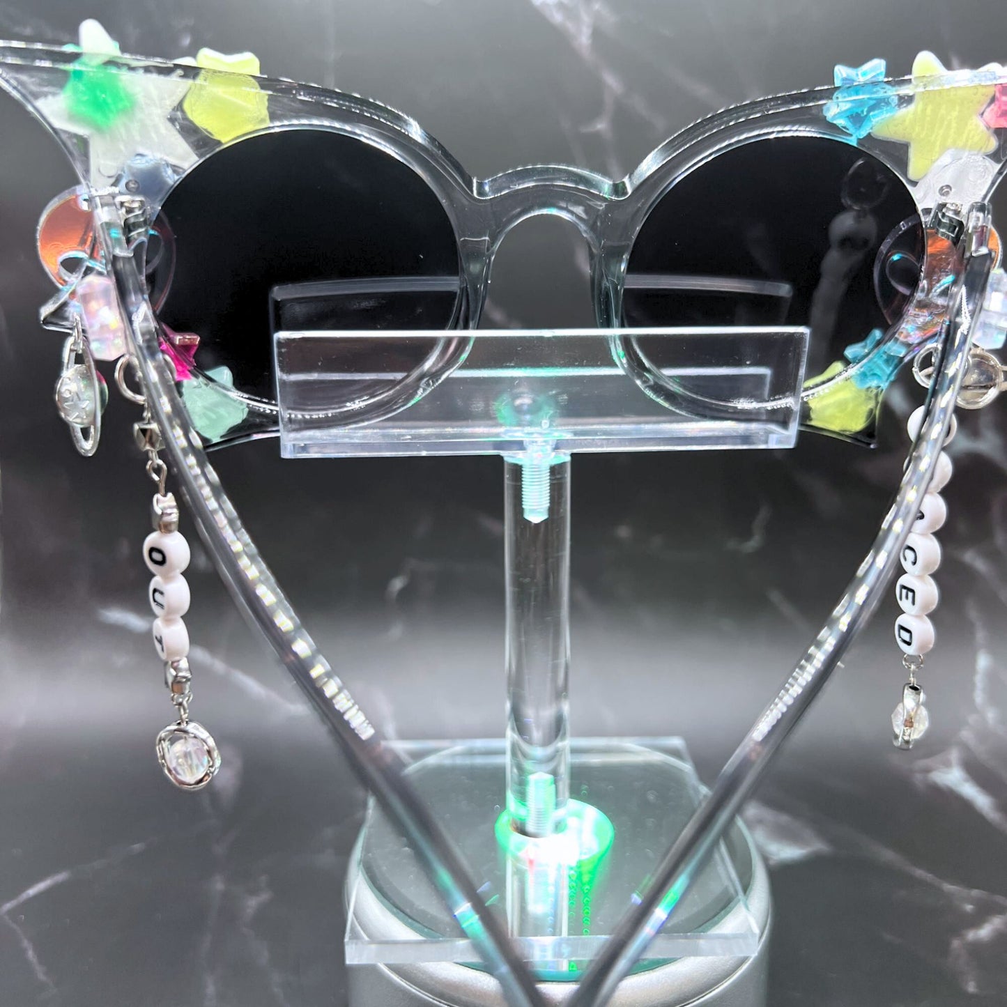 Hypnotic Space Alien Sunglasses with glow-in-the-dark stars and alien charms for a cosmic rave experience! Displayed on a clear stand. Back view.