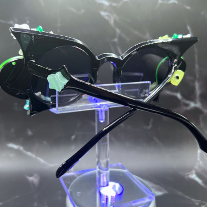 Glow-in-the-dark star festival sunglasses for an out-of-this-world look. Displayed on a clear stand. Back view.