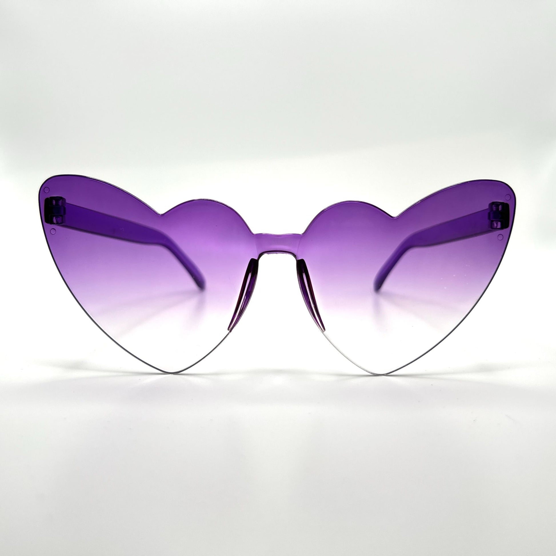 Colorful oversized heart-shaped sunglasses, perfect for festivals and dancing. Lightweight and trendy eyewear for a vibrant and stylish look. Displayed on a table. Front view. Purple Ombre Cat Eye Heart.