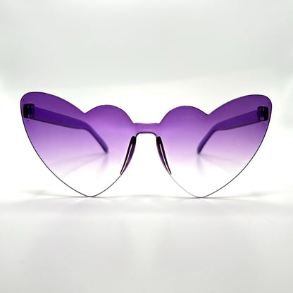 Colorful oversized heart-shaped sunglasses, perfect for festivals and dancing. Lightweight and trendy eyewear for a vibrant and stylish look. Displayed on a table. Front view. Purple Ombre Cat Eye Heart.