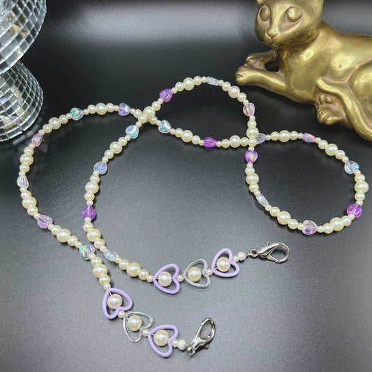 Faux pearl and purple heart beaded glasses chain with silver-tone clasps. Displayed on a table.