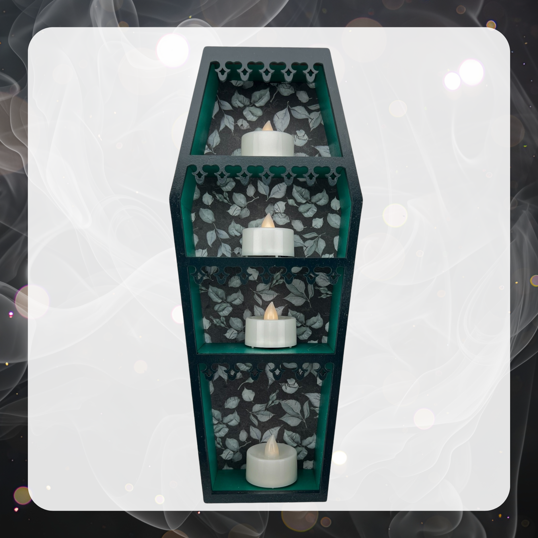 Picture shows a green mini coffin curio shelf with ornate laser cute decorative trim and a back wallpaper printed with white leaves. There are four battery operated tea light candles on each shelf. 