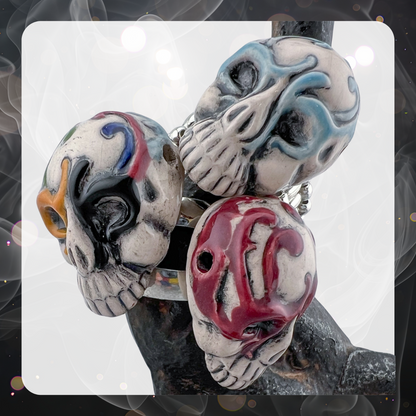 Picture shows three glazed ceramic decorated sugar skulls made into rings. There is a blue one, a red one, and a multi color one that has black, red, yellow, and blue. 