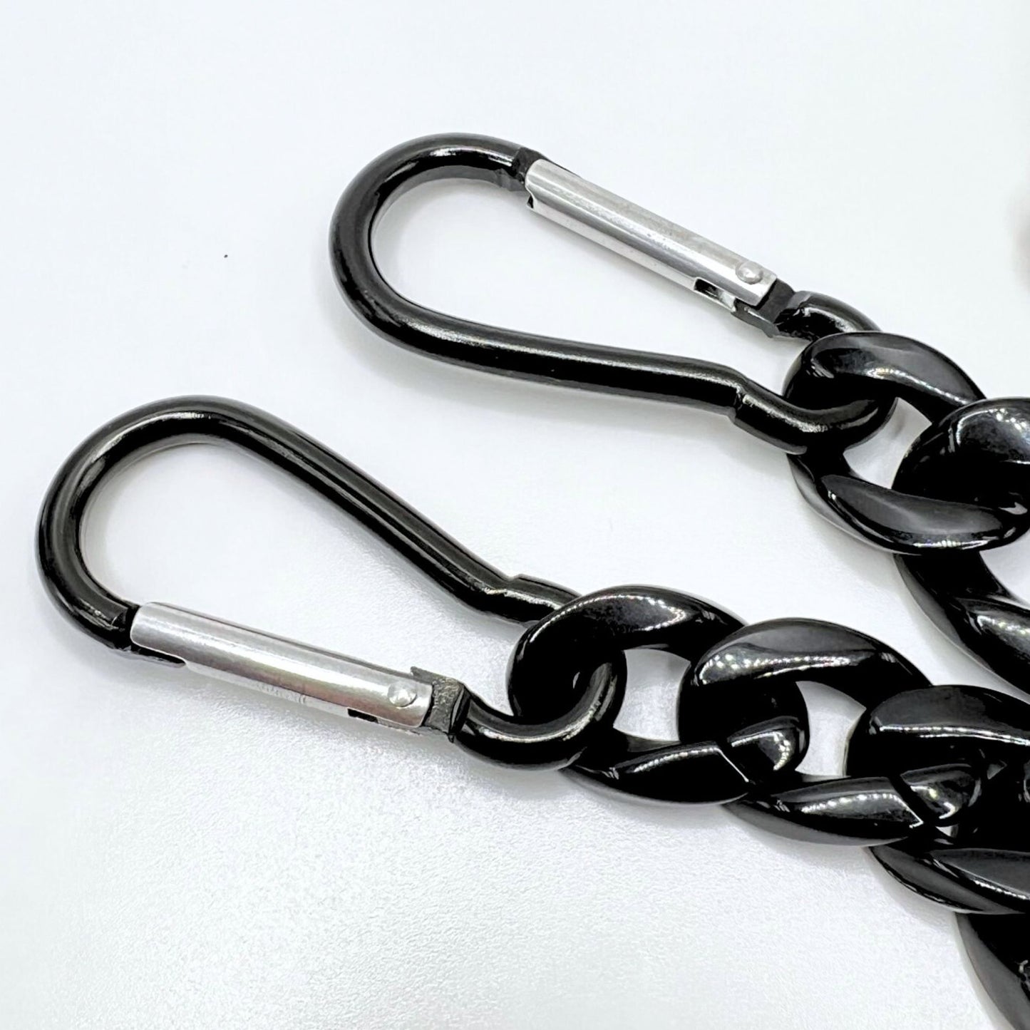 Handmade black acrylic chain with carabiner clips. Displayed on a table. Close up of the carabiners.
