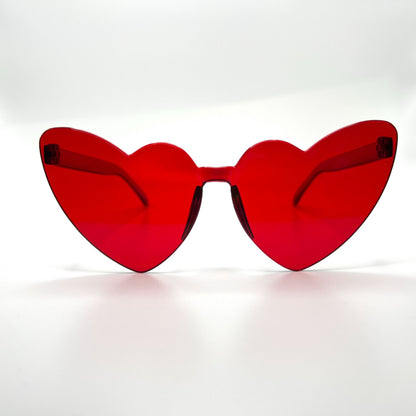 Colorful oversized heart-shaped sunglasses, perfect for festivals and dancing. Lightweight and trendy eyewear for a vibrant and stylish look. Displayed on a table. Front view. Red Cat Eye Heart.