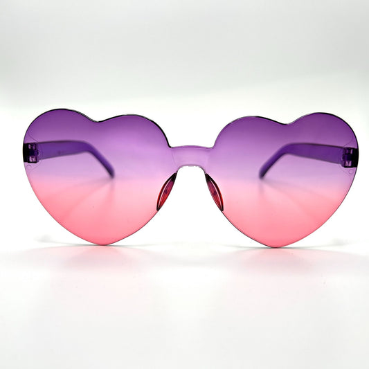 Colorful oversized heart-shaped sunglasses, perfect for festivals and dancing. Lightweight and trendy eyewear for a vibrant and stylish look. Displayed on a table. Front view. Purple Pink Ombre Heart.