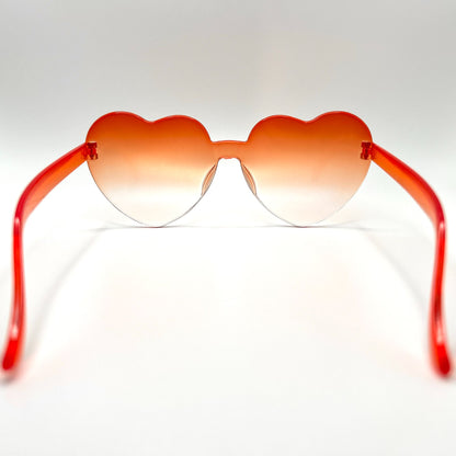 Colorful oversized heart-shaped sunglasses, perfect for festivals and dancing. Lightweight and trendy eyewear for a vibrant and stylish look. Displayed on a table. Back View. Orange Ombre Heart.