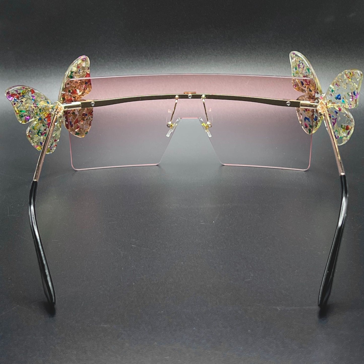 Butterfly Shield Sunglasses – Oversized and enchanting eyewear for standing out at festivals and raves. Displayed on a table. Back view.