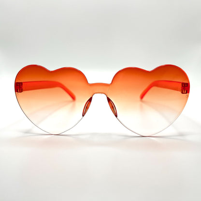 Colorful oversized heart-shaped sunglasses, perfect for festivals and dancing. Lightweight and trendy eyewear for a vibrant and stylish look. Displayed on a table. Front view. Orange Ombre Heart.