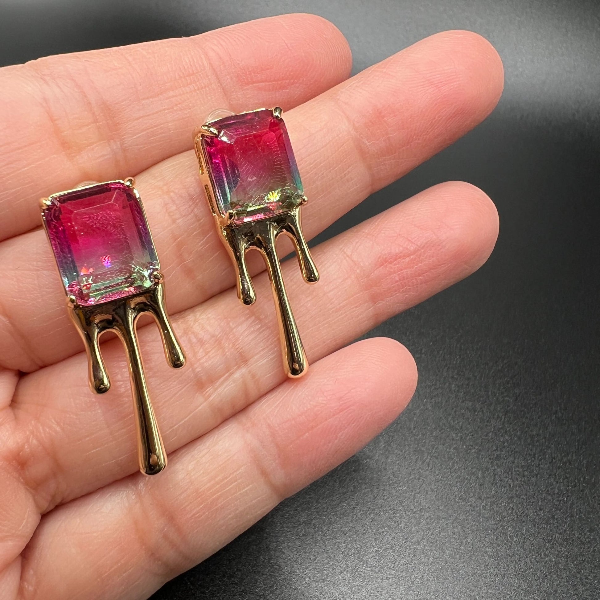 Gold metal earrings with melted design and large pink/green imitation watermelon tourmaline stones. Displayed on a hand with a close-up view of  the gems.