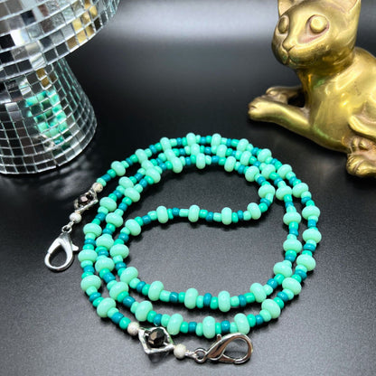 Mint blue and green beaded glasses chain with silver-tone clasps. Displayed on a table.